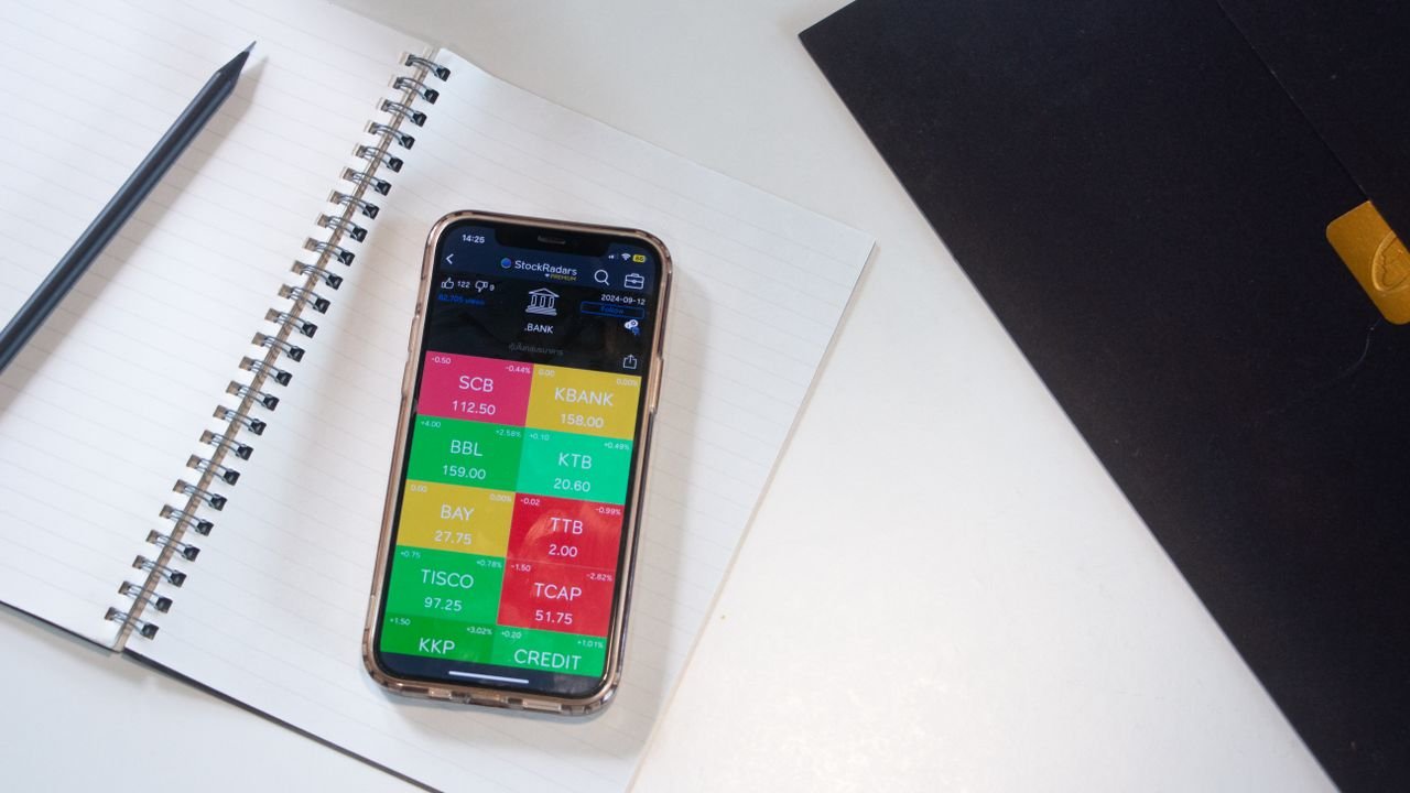 services-02 A smartphone displays a financial stock market app on a desk with a notebook and pencil.