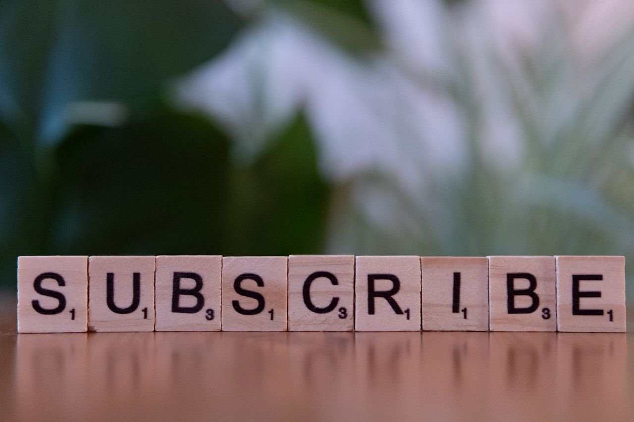 services-03 Close-up of the word 'SUBSCRIBE' spelled with wooden letter tiles on a table.